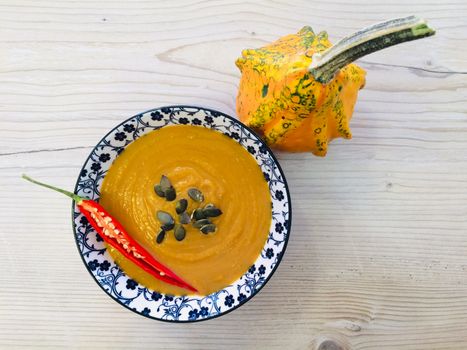 Delicious pumpkin soup garnished with chili pepper and seeds next to an ornamental gourd.