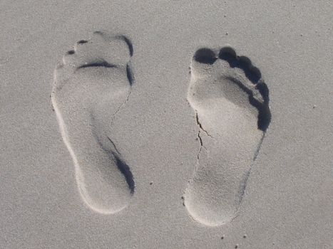Close-up of two footprints imprinted in smooth beach sand.