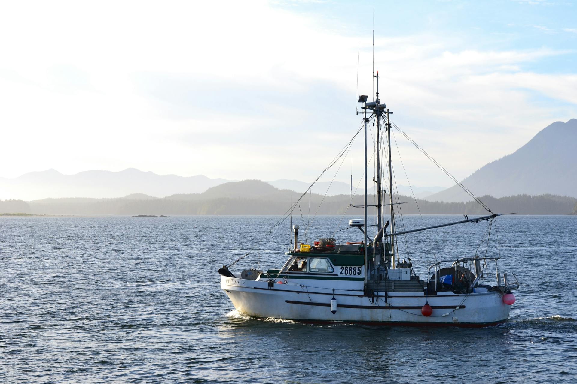 A lone commercial fishing boat navigating calm waters with mountain backdrop.