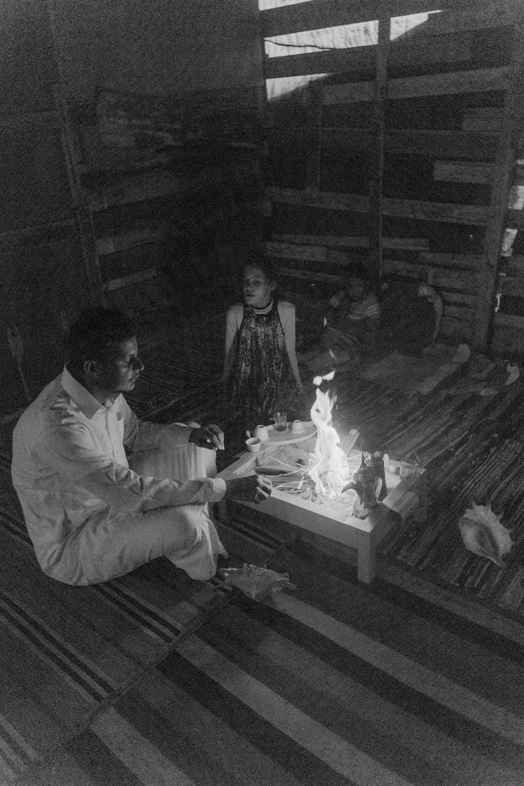 Black And White Photo Of A Man Cooking At The Table While Sitting Beside A Woman