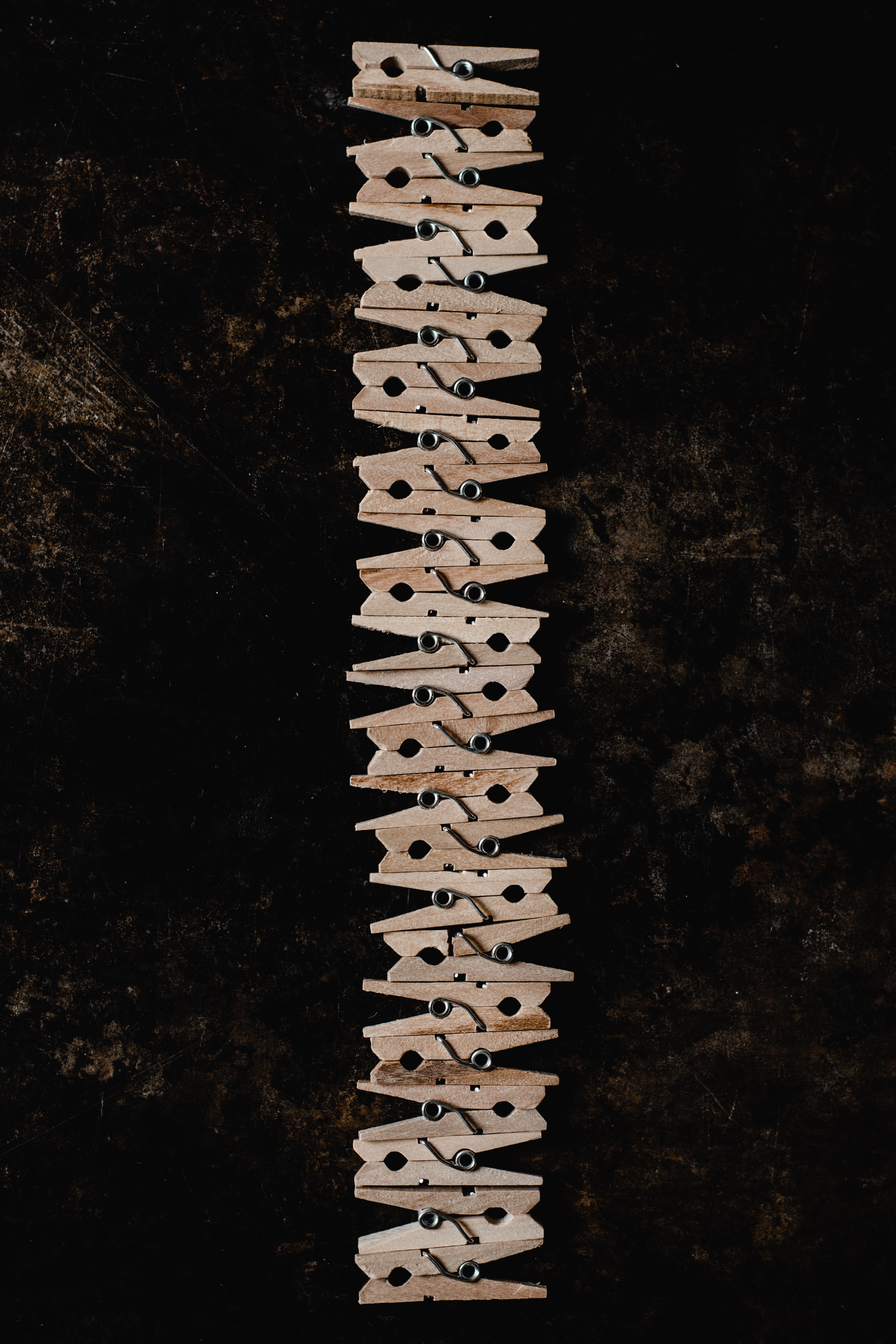 A neatly aligned vertical row of natural wood clothespins against a textured dark background.