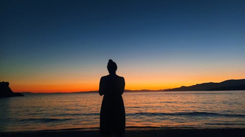 Silhouette of Woman Standing on a Beach at Sunset