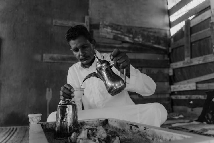 A Man In A Thobe Pouring Tea From A Kettle