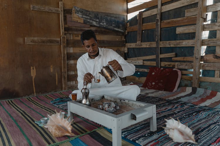 A Man In A Thobe Pouring Tea From A Kettle