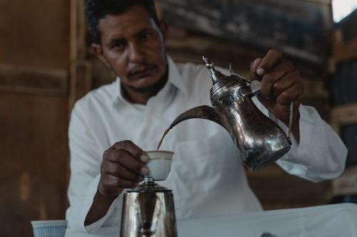 Free A man pours coffee from a traditional pot in an authentic Middle Eastern setting. Stock Photo
