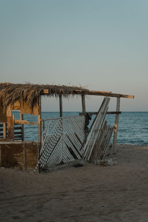 Free Rustic wooden hut on a sandy beach with calm ocean backdrop, capturing a peaceful evening atmosphere. Stock Photo
