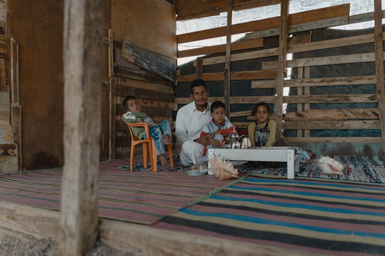 A Man Sitting In A Shack With His Children