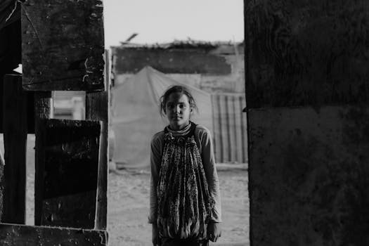A captivating black and white portrait of a young girl standing in a rustic environment, evoking a sense of solitude and strength.