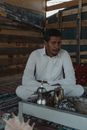 A Man in a White Outfit Sitting in front of Stainless Kettles