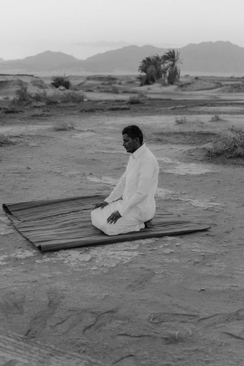 Grayscale Photo of a Man Praying in the Desert