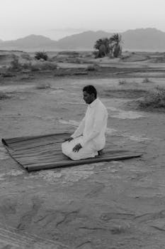 A man in prayer kneeling on a mat in a vast desert landscape.