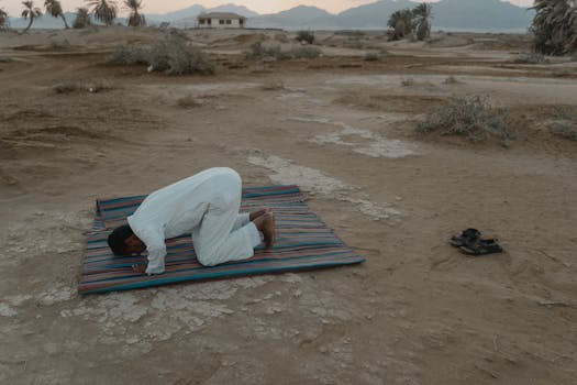 A Muslim man kneels in prayer on a colorful mat in the desert during sunset, showcasing a serene moment of faith.