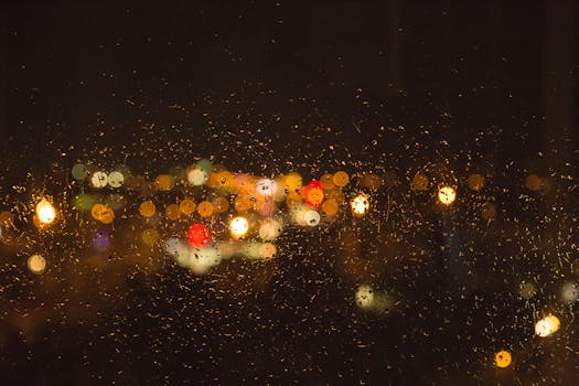 Beautiful bokeh of city lights through a rain-covered window, capturing an urban nighttime scene.