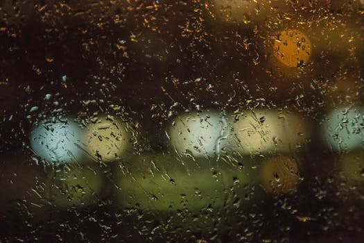 Glass window with tiny droplets from rain and bright lights of modern megalopolis