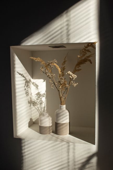 Elegant still life of dried wildflowers in vases casting shadows on an interior wall.