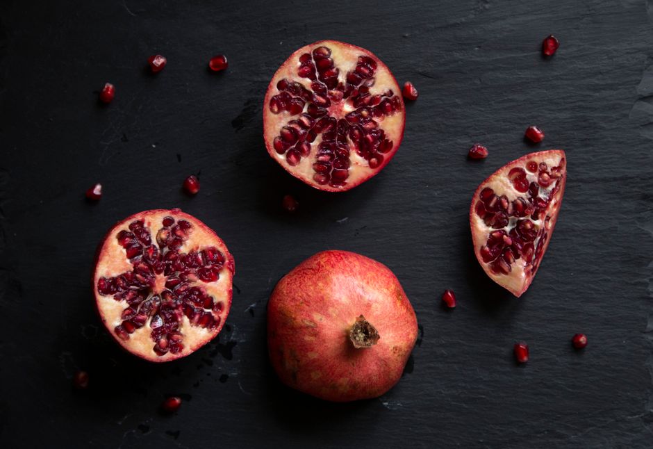 Close-up of fresh pomegranate slices and seeds on a dark slate surface, highlighting their vibrant color and texture.