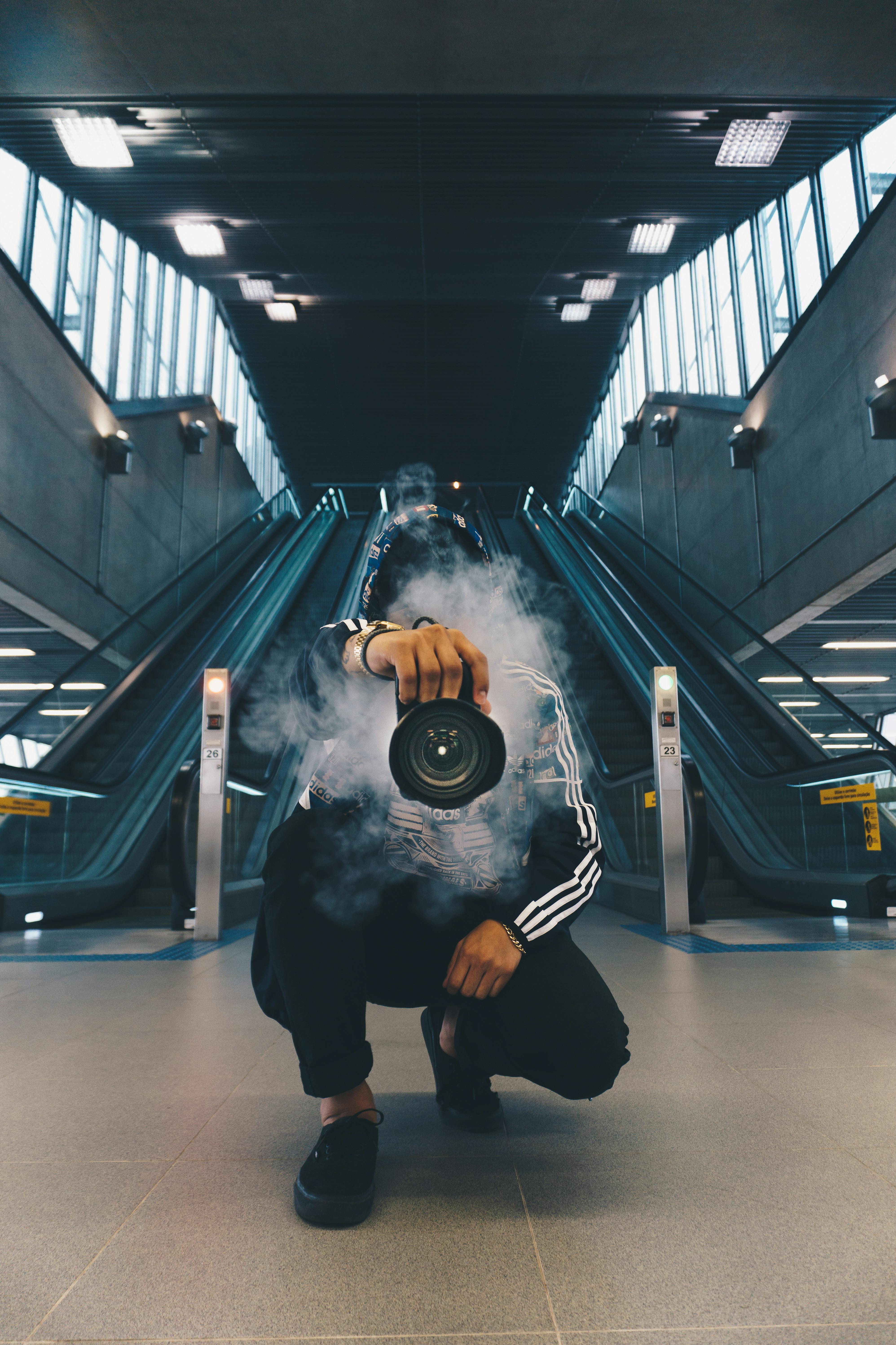 man holding camera while squating with smoke on face inside building