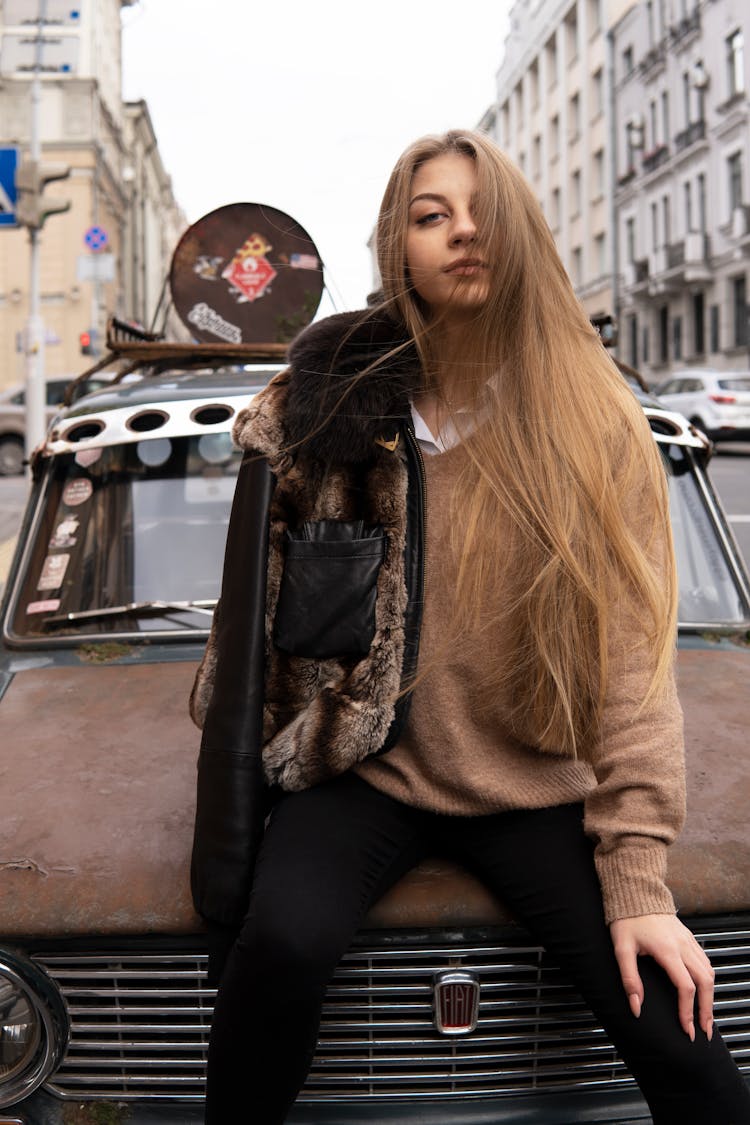 A Woman In A Sweater Sitting On A Car Hood 