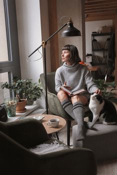 女人在舒适的客厅里，一边看书一边逗猫，享受着放松的时光