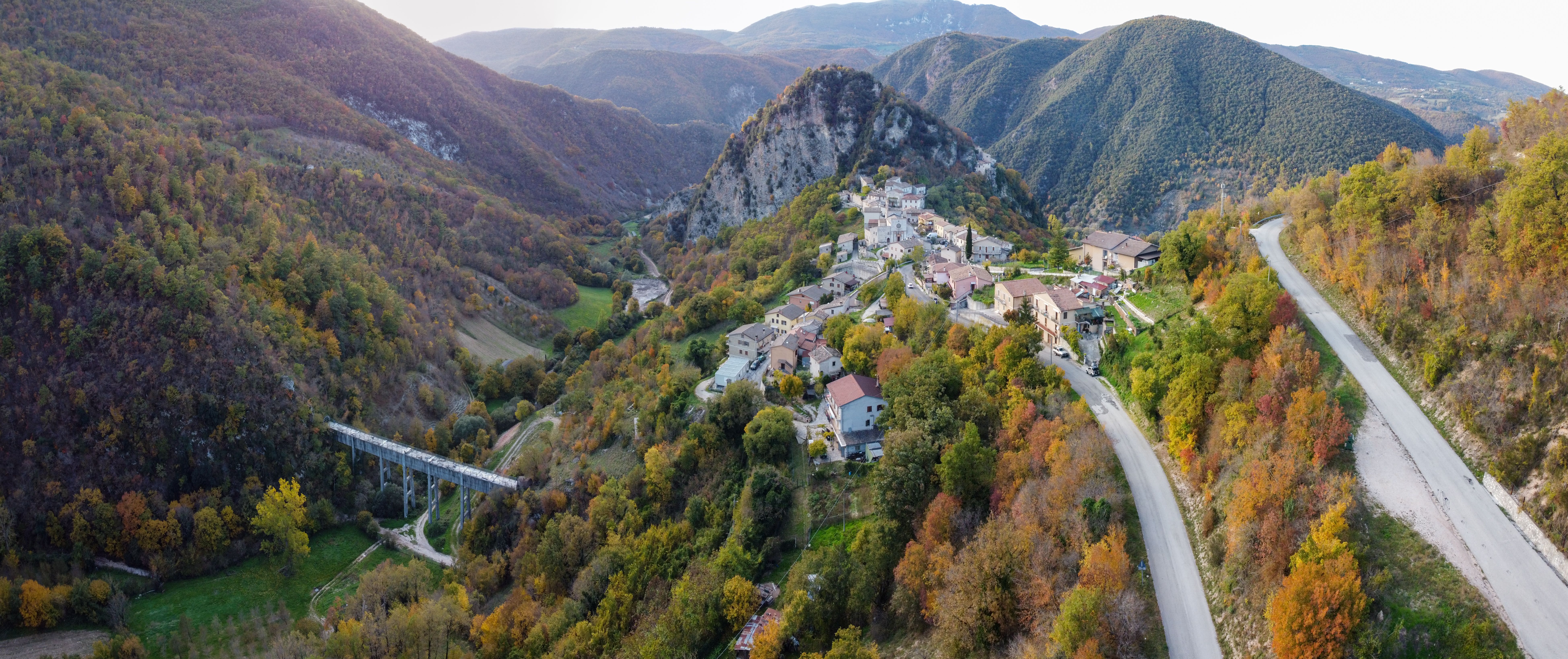 Picturesque scenery of small remote settlement located on hilltop surrounded by lush green hills on early autumn day