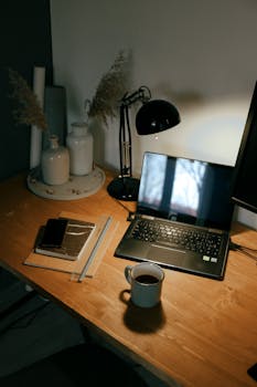 A warm-toned workspace featuring a laptop, coffee cup, and notebooks on a wooden desk.