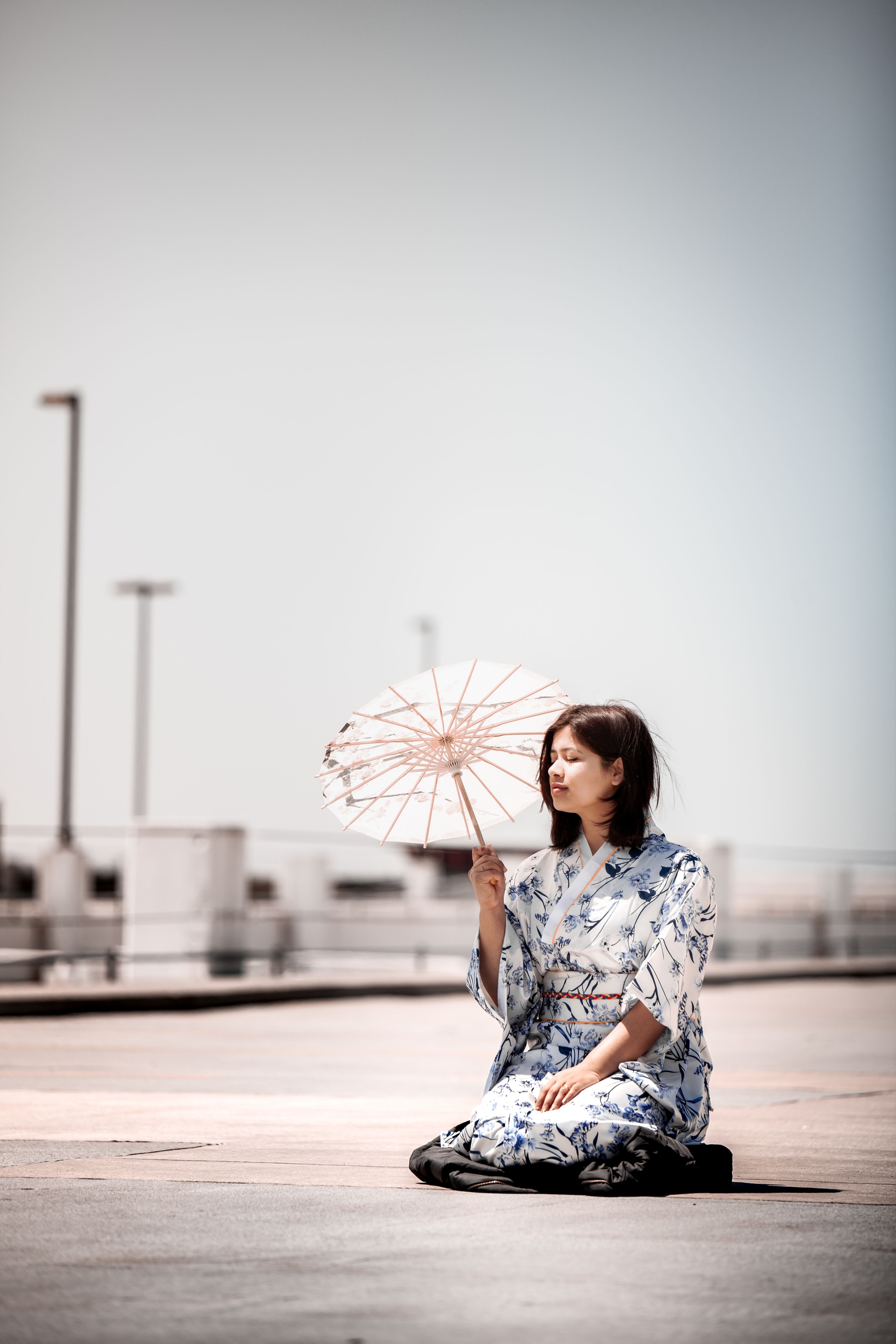 一位穿着和服的优雅女子跪在户外明亮的阳光下，举着和笠遮阳伞