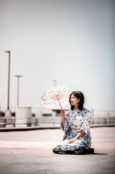 一位穿着和服的优雅女子跪在户外明亮的阳光下，举着和笠遮阳伞