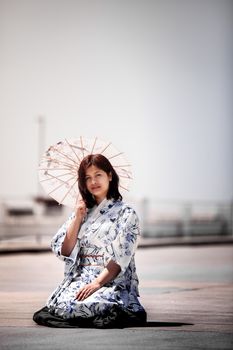 阳光明媚的户外，一名身穿和服的妇女跪在地上，举着日本传统伞