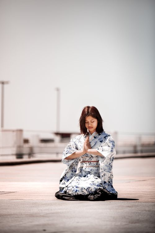 Free Asian woman in traditional kimono kneeling and praying outdoors, embodying tranquility. Stock Photo
