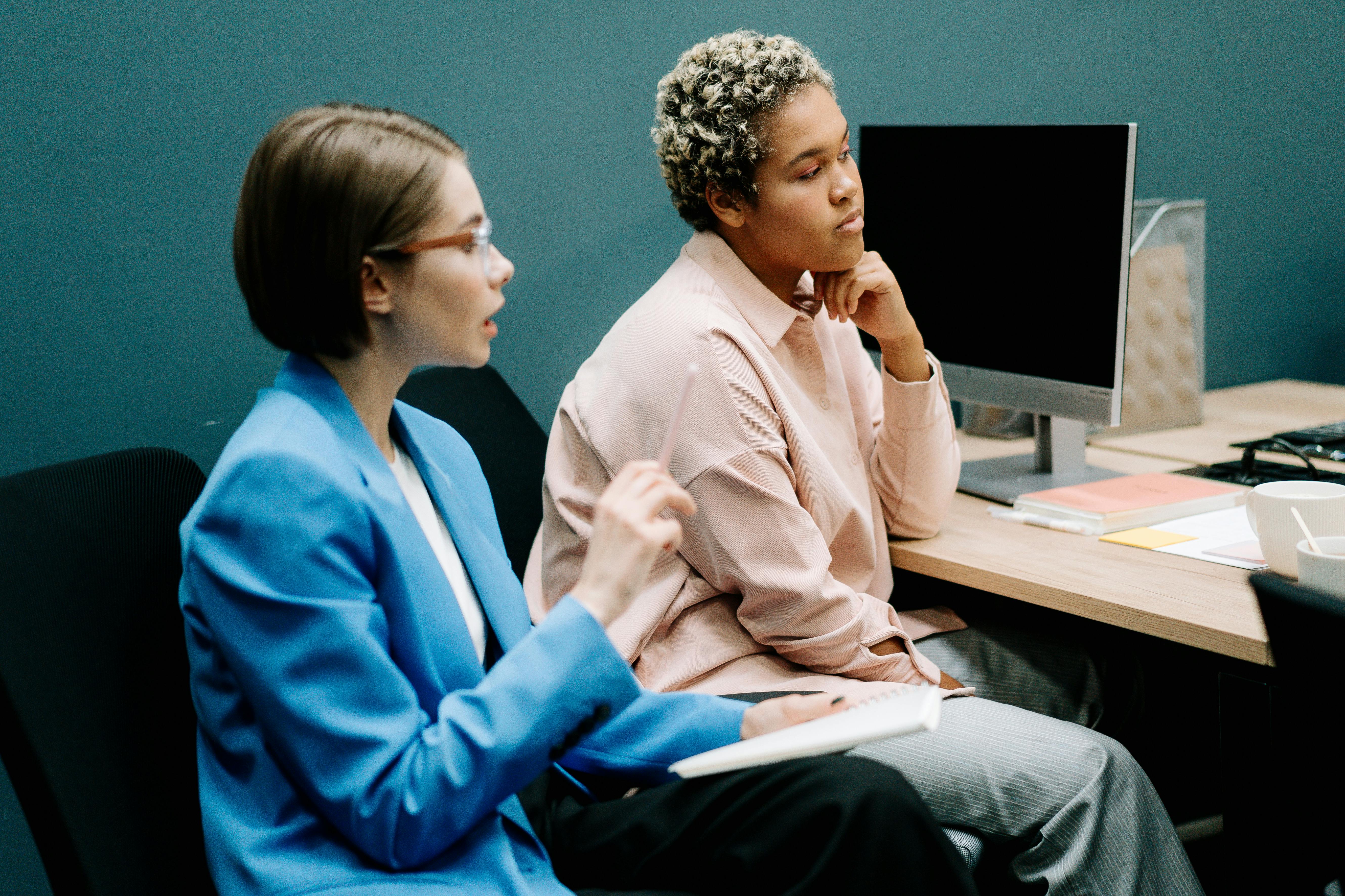 woman in blue dress shirt sitting beside woman in white dress shirt