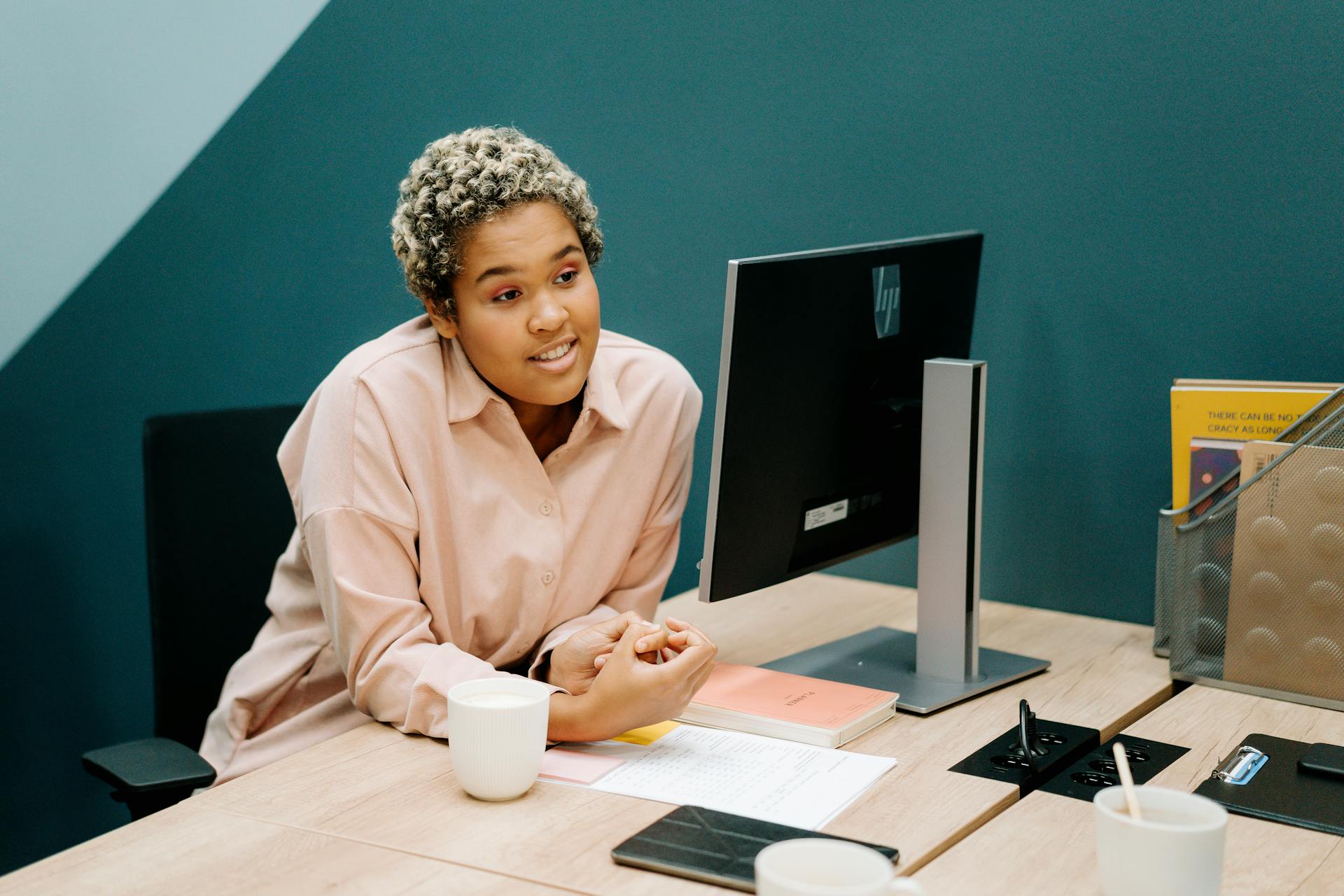 Professional woman in office, discussing work at her desk with desktop computer.