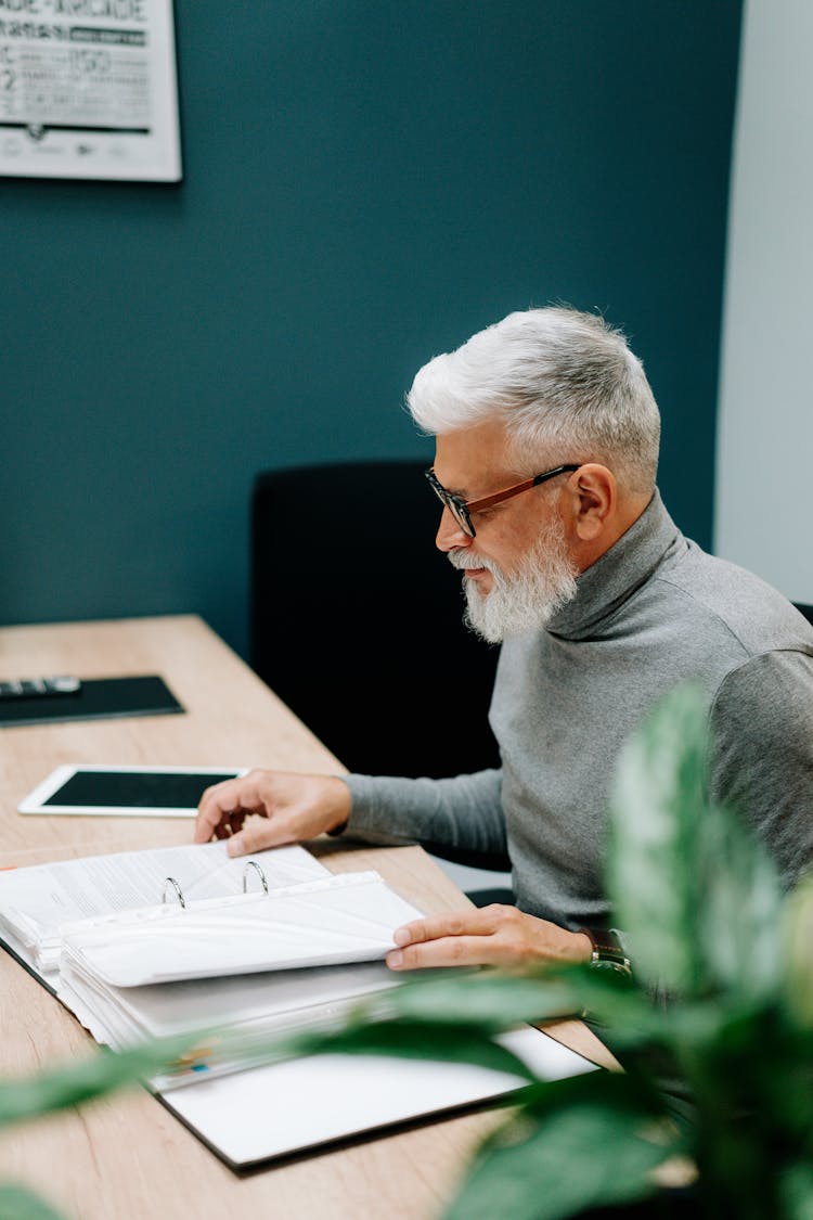 An Elderly Man Reading Documents In The Office