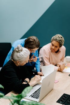 Three diverse colleagues discussing work over a laptop in a modern office setting.