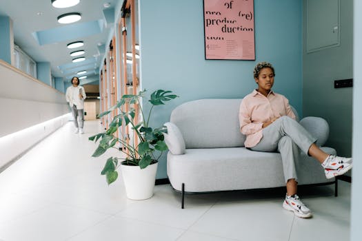 A woman sits on a sofa in a bright, modern office hallway, creating a relaxed atmosphere.