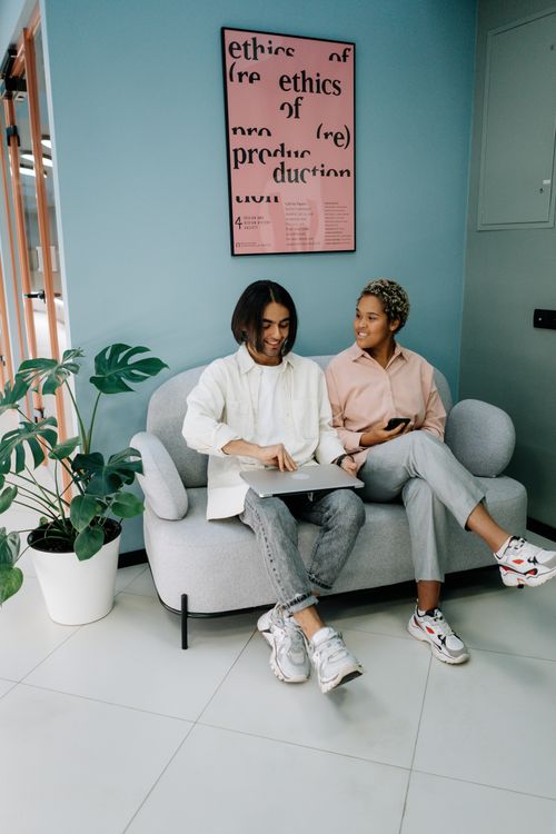 Free Two young adults discussing work on a sofa in a stylish, contemporary office lobby. Stock Photo