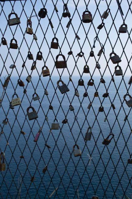 Padlocks on a fence in Dubrovnik with a serene Adriatic Sea backdrop, symbolizing love and commitment.