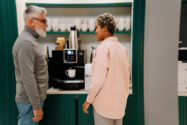 A Man And Woman Having Conversation While Standing Near The Coffee Machine