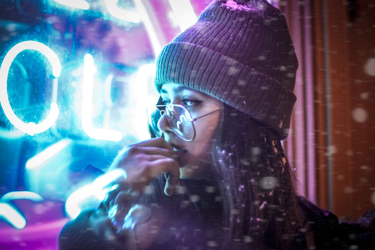 Woman wearing a beanie and glasses near neon lights in snow