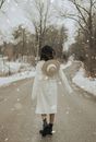 Back view of anonymous trendy female with hat on wet road while snowing