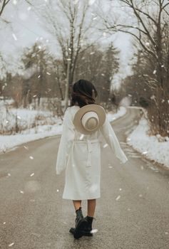 一位戴着帽子的时髦女性在雪中湿路上的背影