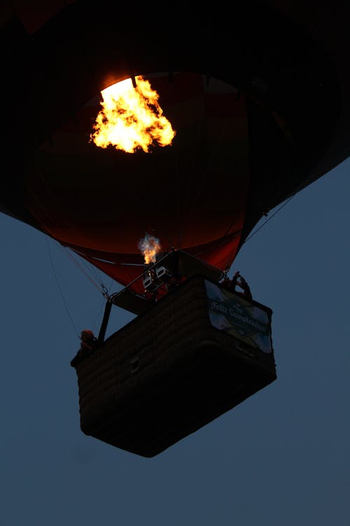 From below of air balloon with bright burning fire flying in cloudless evening sky