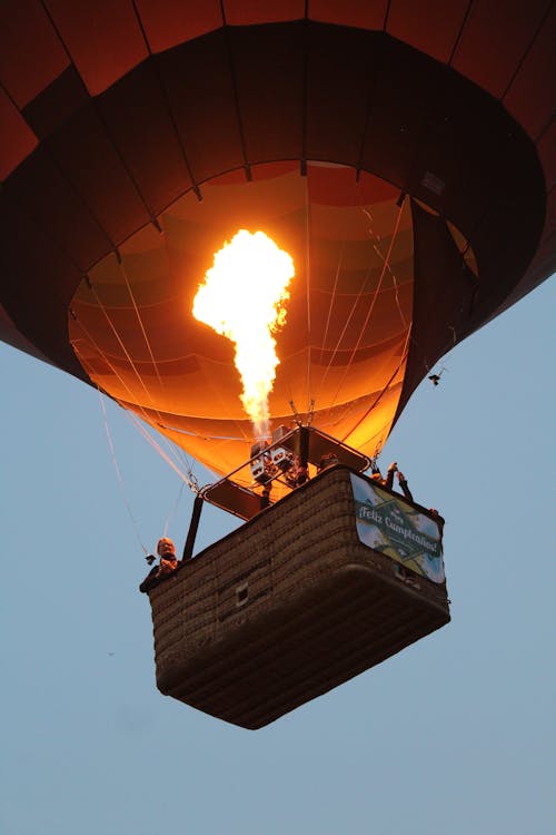 From below of hot air balloon with bright burning flame flying in cloudless evening sky