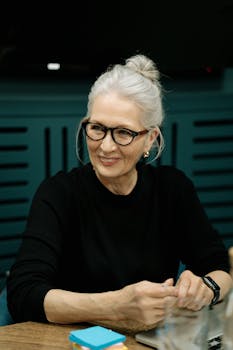 Elderly woman with gray hair wearing eyeglasses during a business meeting indoors.