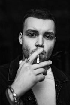 Monochrome portrait of a young man smoking a cigarette, showcasing a moody and dramatic atmosphere.