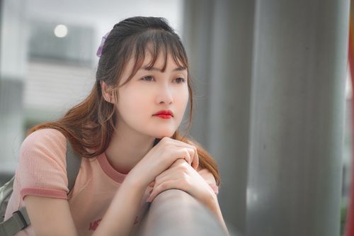 Free A young woman with red lips thoughtfully leans on a handrail indoors, with a blurred background. Stock Photo