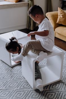 Two children having fun and playing with a modern white coffee table in a cozy living room.