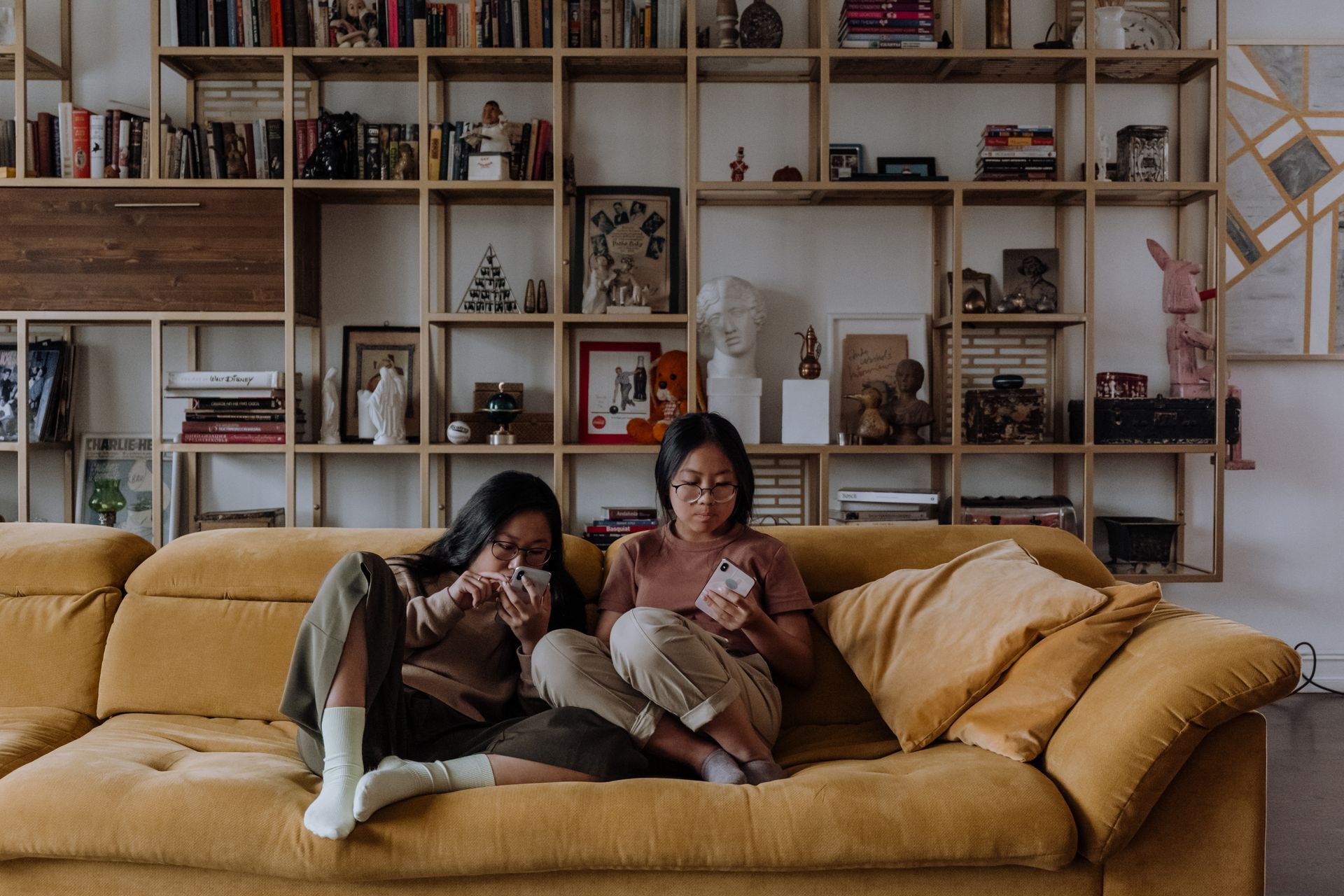 Two teenage siblings using smartphones while sitting on a cozy sofa in a stylish living room.