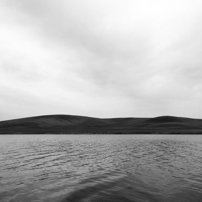 Monochrome image capturing a tranquil water body and rolling hills.