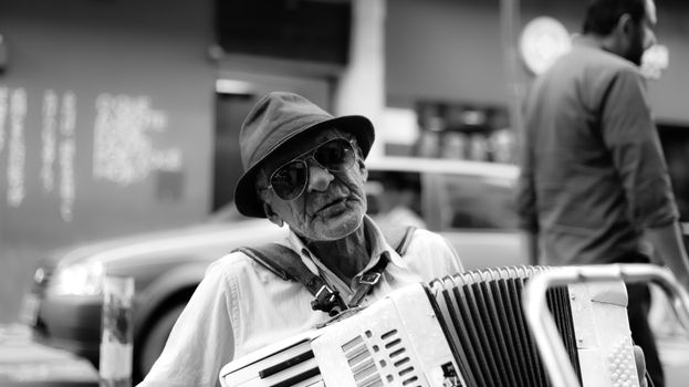 Black and white photo of an elderly musician playing accordion on the street.