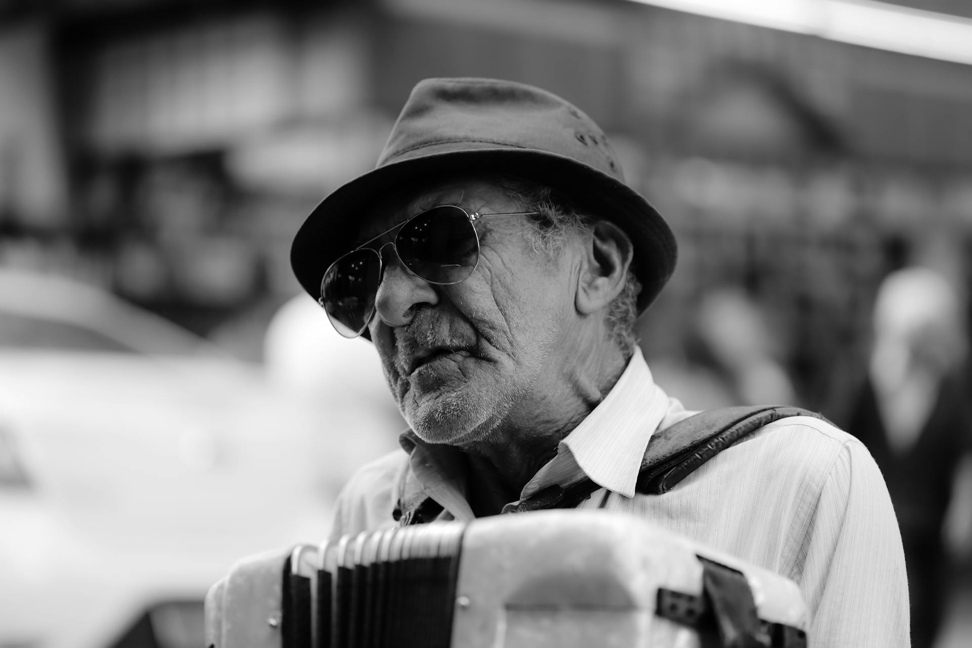 Black and white portrait of a senior man with sunglasses playing an accordion outdoors.